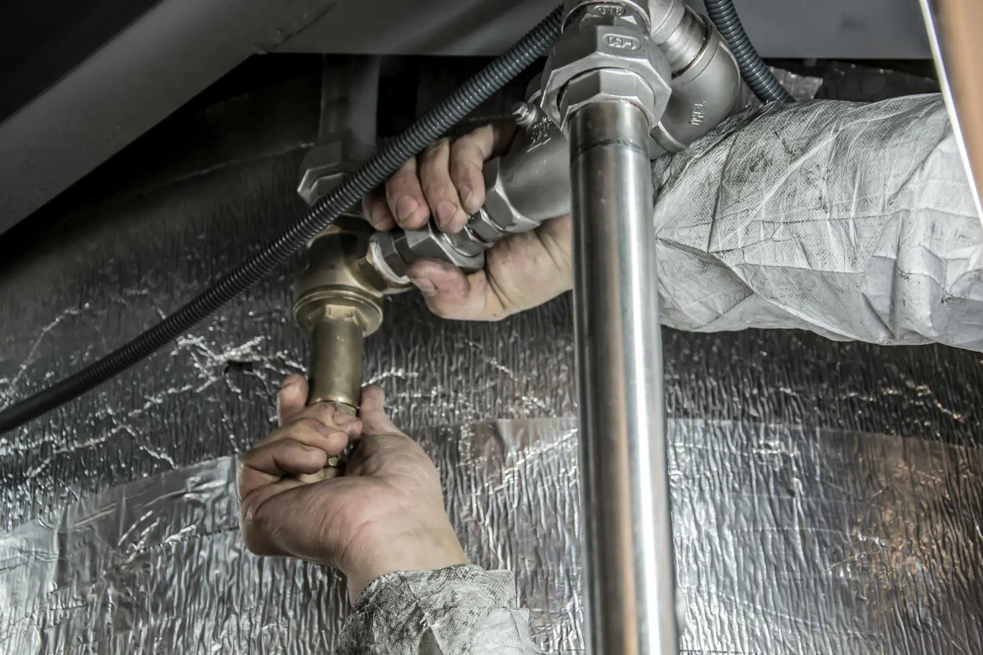 Plumber working on copper and brass pipework under a sink in Sheffield